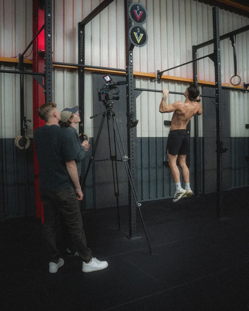Camera on a tripod during a gym shoot in Switzerland while Lua Hell and a crew member watch the frame