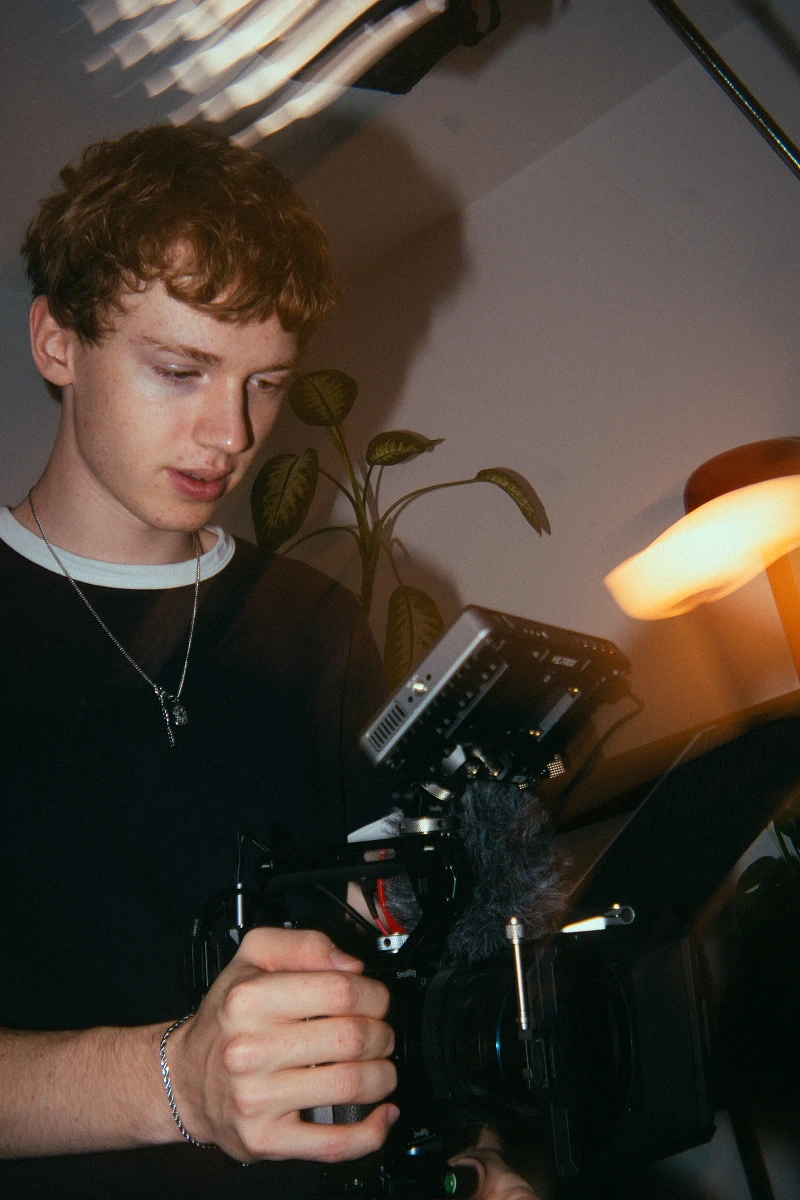 Filmmaker Lua Hell operating a handheld cinema camera in warm lamp light during an indoor shoot