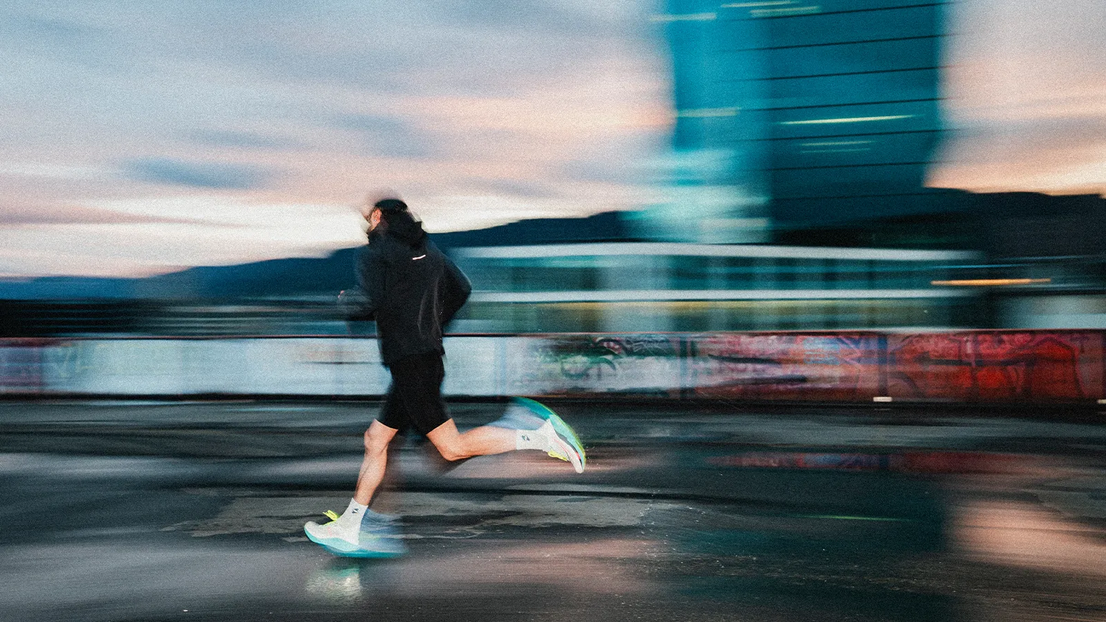 Behind the scenes from Saucony The Run commercial: motion-blurred frame of a runner passing a graffiti wall with the Zurich skyline at golden hour, captured by filmmaker Lua Hell